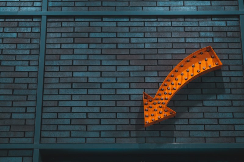 An orange marquee arrow sign on a brick wall