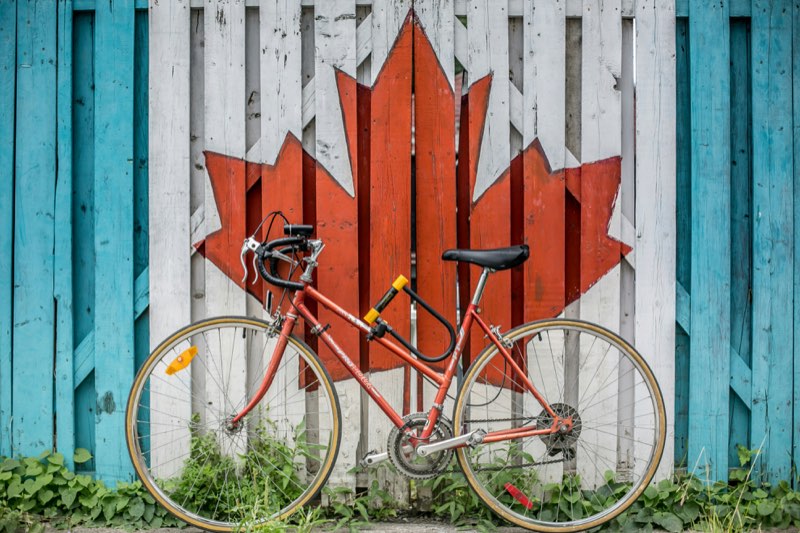 A red bike leaning on a fence painted with a Canadian maple leaf
